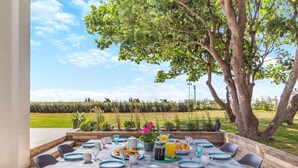 Un espace de restauration en plein air avec une table dressée pour quatre personnes, entourée de chaises, et offrant une vue sur un champ verdoyant et des arbres.