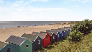 Une rangée de cabanes de plage colorées s’étend le long d’une plage de sable, offrant une vue sur la mer.