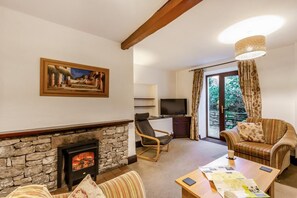 A living room with a stone fireplace, a television, a sofa, a chair, and a table with papers. - 2 Bed in Newby Bridge (oc-o28384) (Newby Bridge)