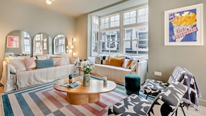 Ein gemütliches Wohnzimmer mit Sofa, Sesseln, einem Couchtisch und einem großen Fenster mit Blick auf die Stadt.