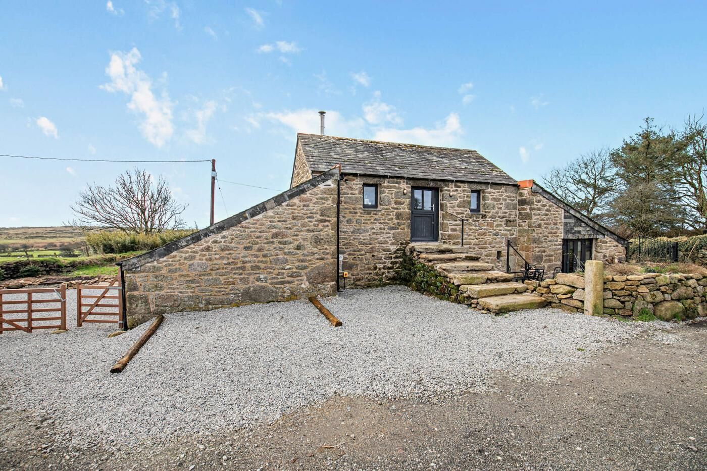A stone cottage with a steeply pitched roof, a small porch, and a gravel driveway.