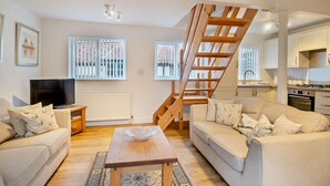A living room with a TV, two sofas, a coffee table, a wooden staircase, and a kitchen area. - 2 Bed in Bodham (oc-m15008) (Bodham)