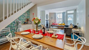 A dining area with a wooden table set for four, white chairs, and a staircase with a white railing. - 2 Bed in Whitstable (oc-f28381) (Whitstable)