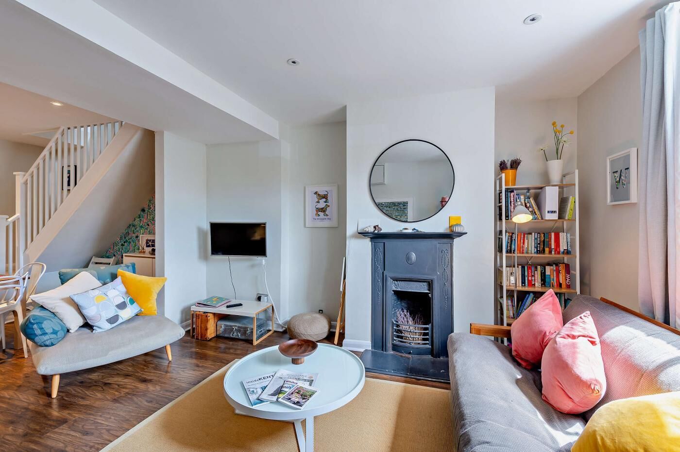 Ein modernes Wohnzimmer mit Kamin, Fernseher, Bücherregal und einer Treppe.