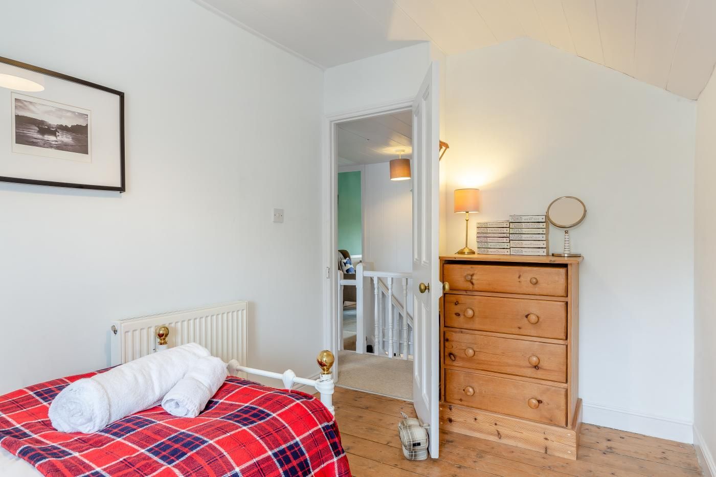 Un dormitorio con cama, cómoda, un cuadro enmarco y una puerta que da a otra habitación.