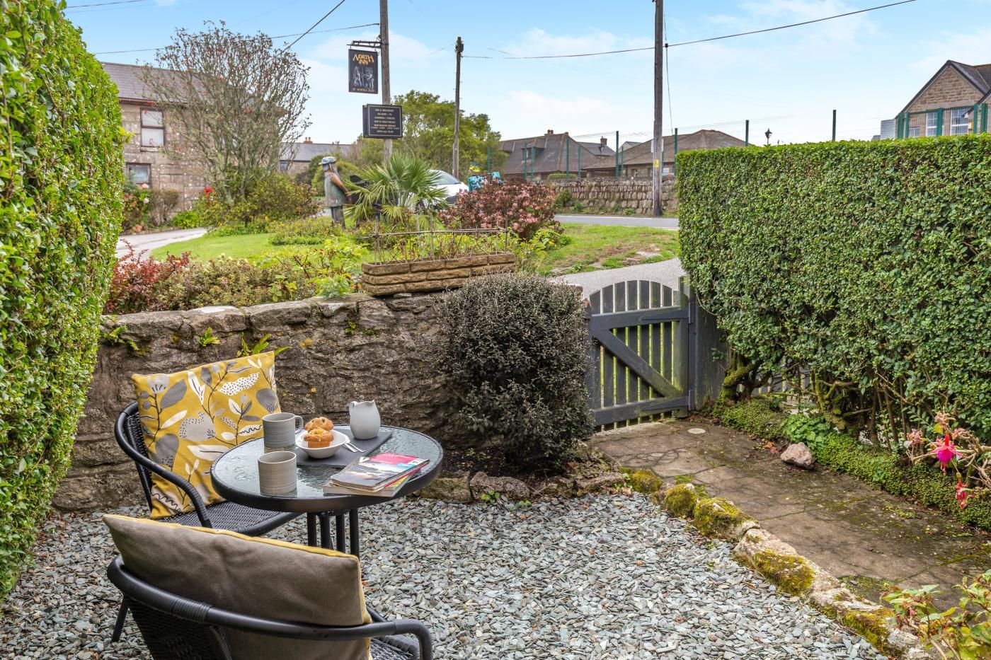 A patio area with a table and chairs, a stone wall, and a hedge.