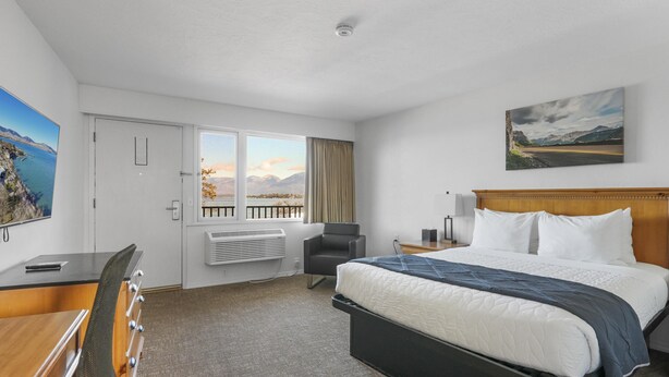 A hotel room with a bed, a desk, a chair, a window with a view, and a painting on the wall.