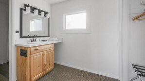 A bathroom with a wooden vanity, a mirror with lights, a window, and a towel rack.