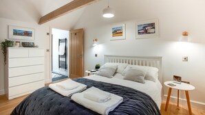 Et soveværelse med seng, sengebord, skab, dør og et loft med synlige bjælker.