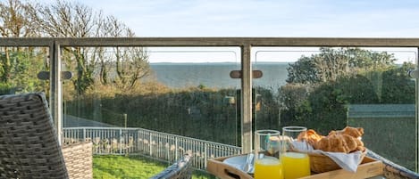 A balcony with wicker furniture, a glass table, and a tray with bread and orange juice.
