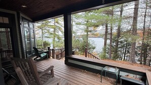 A wooden deck with outdoor seating and a view of a lake surrounded by trees.