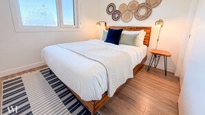 A bedroom with a bed, a bedside table, a standing lamp, a window, and a wall with decorative items. - The Cache Contemporary DT Condo (Golden)