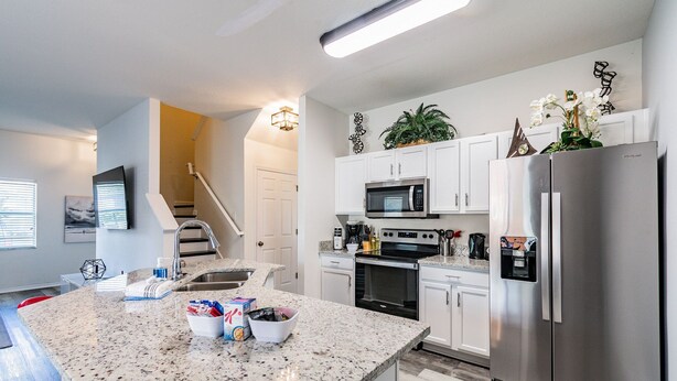 A modern kitchen with granite countertops, stainless steel appliances, and white cabinetry. - 4BR Townhome w/ Pool in Bella Vida Resort (Kissimmee)