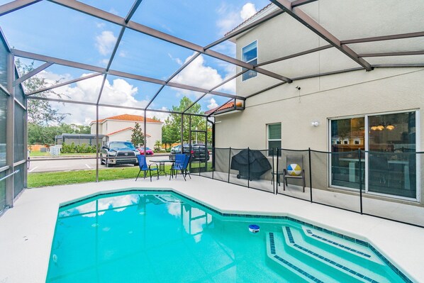 Una piscina con cerramiento de vidrio, mobiliario exterior y vista a la calle.