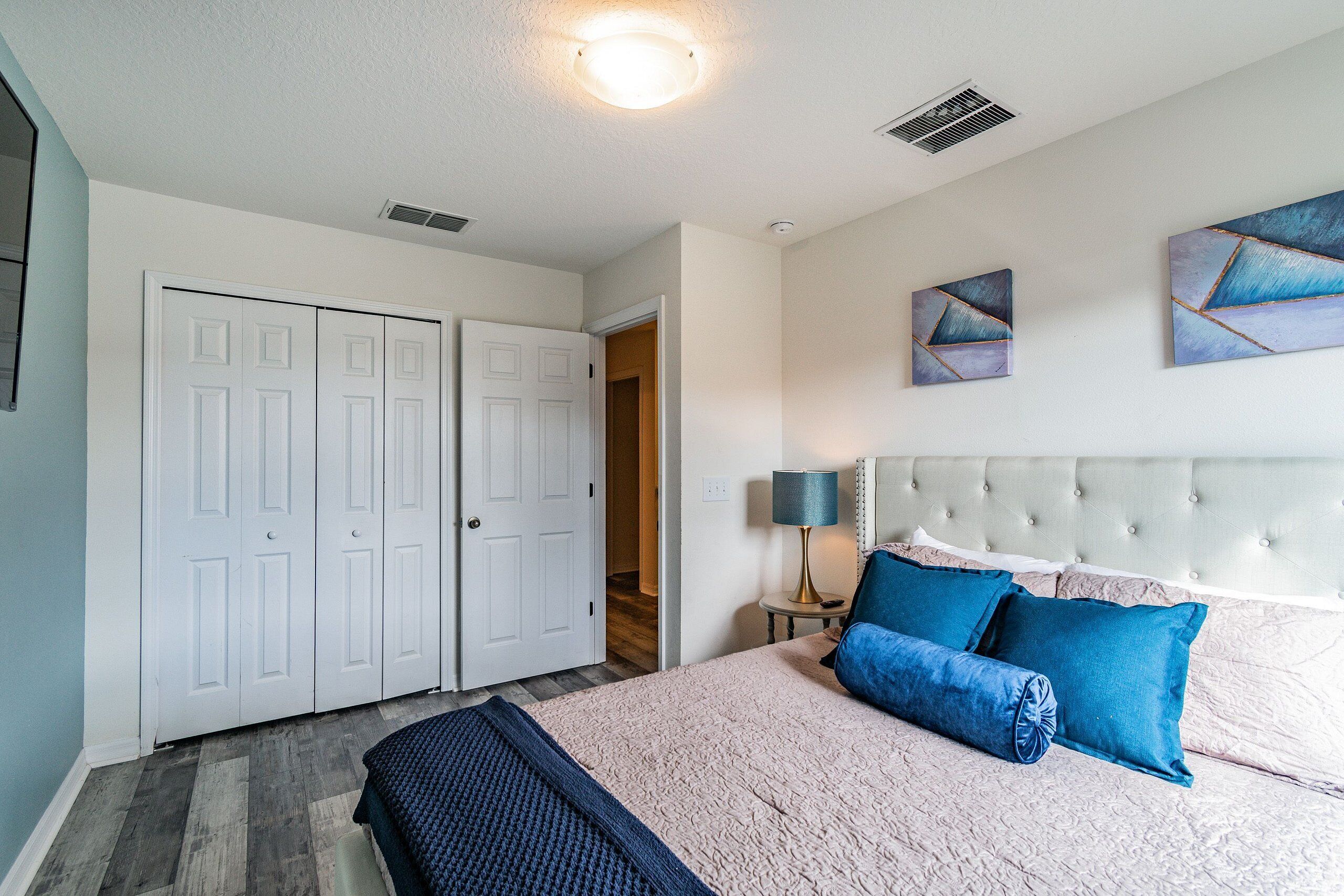 A bedroom with a bed, a nightstand, a lamp, and a wall with two paintings.