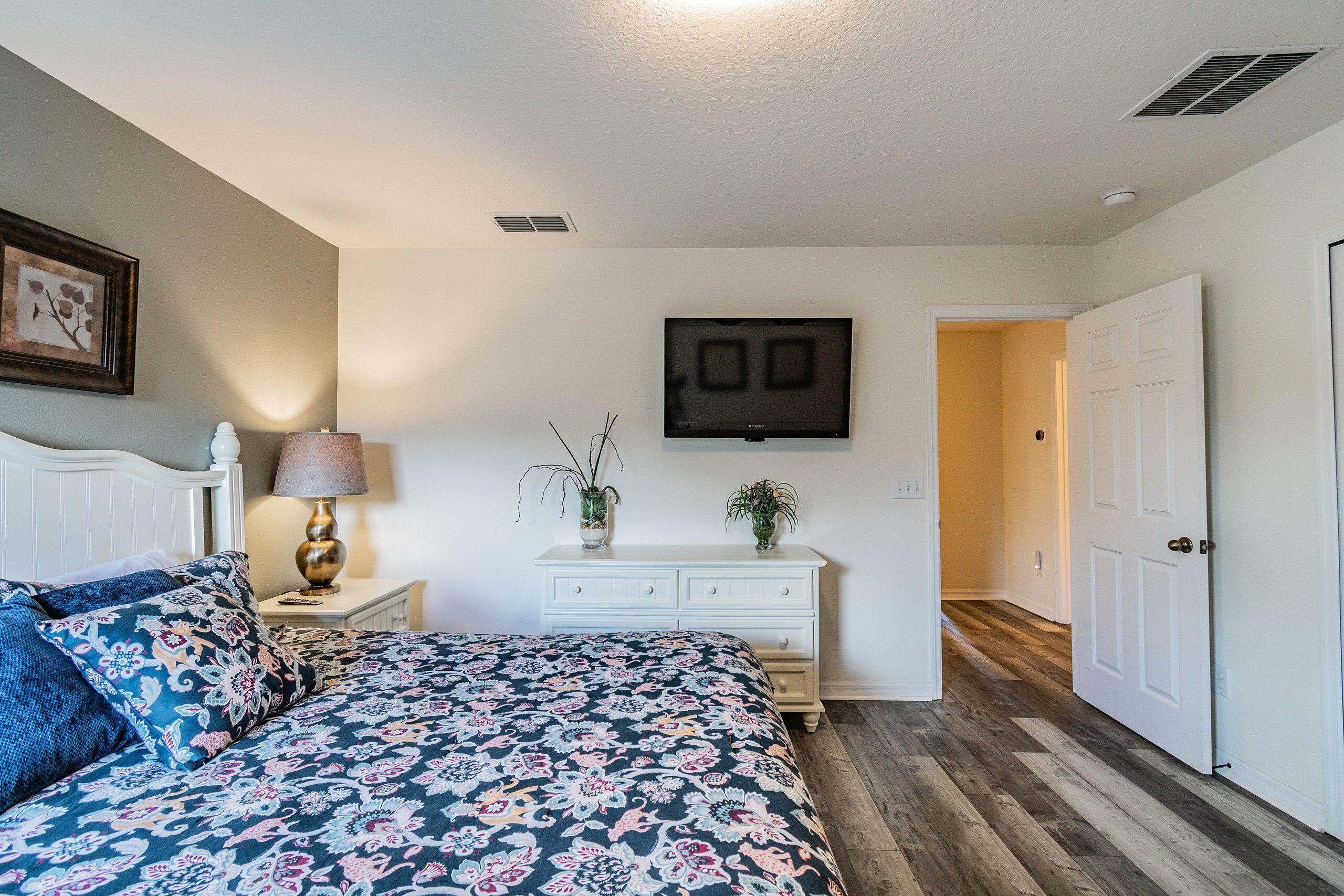 A bedroom with a bed, a dresser, a TV, and a door leading to another room.