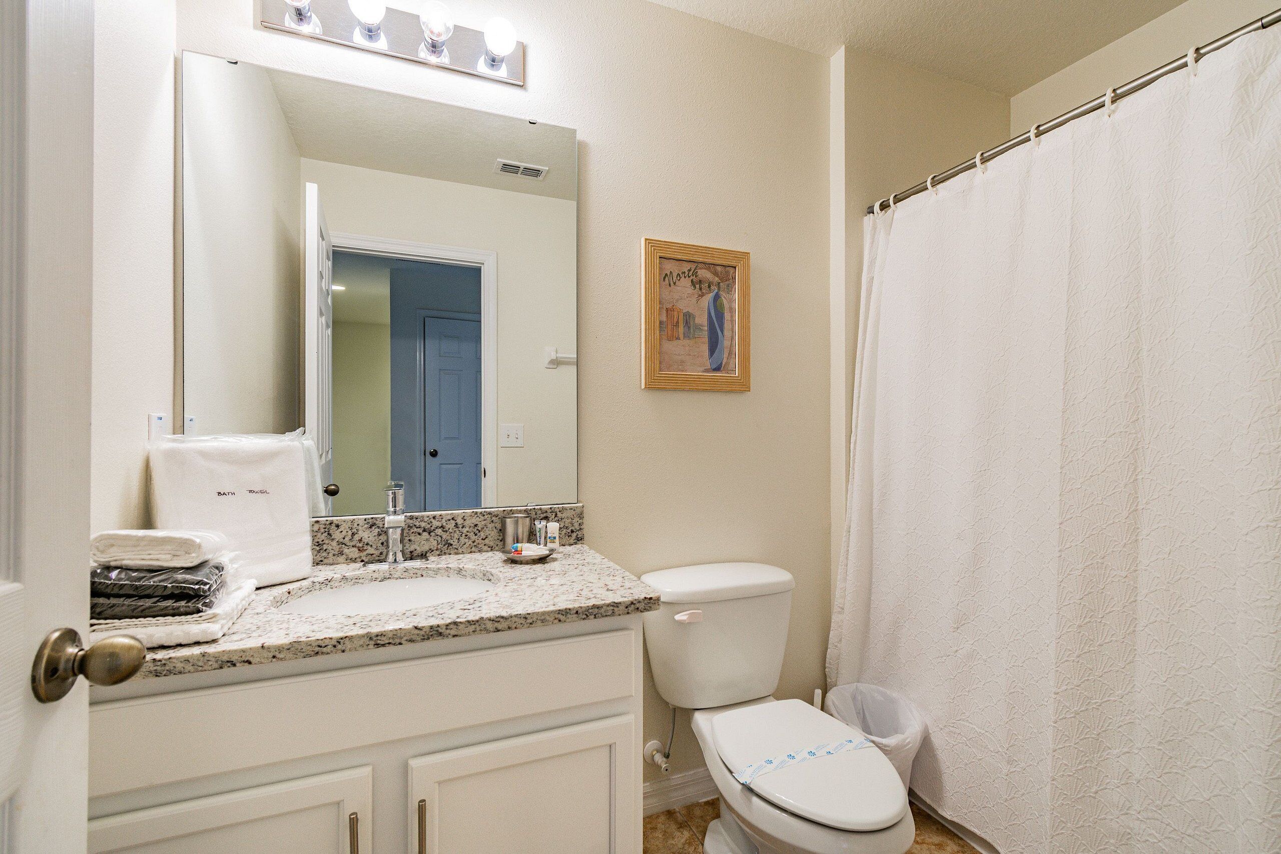 Une salle de bain avec des toilettes blanches, un lavabo surmonté d’un miroir et un rideau de douche.