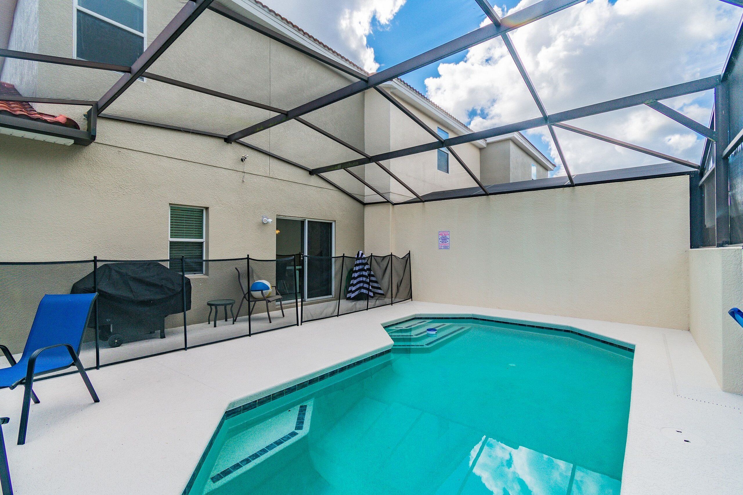 An outdoor swimming pool with a covered patio area, a blue chair, and a grill.