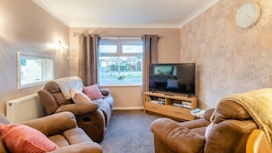 A living room with a sofa set, a television on a wooden stand, a radiator, and a window with curtains. - 2 Bed in Holt (oc-r28378) (Holt)