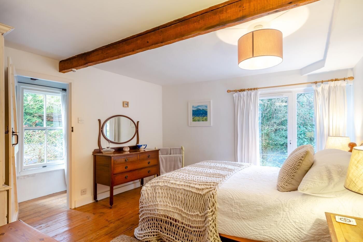 A bedroom with a wooden bed, a dresser, a mirror, and a window with curtains.