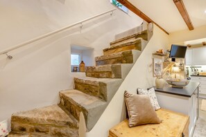 A stone staircase leading to a kitchen with a TV, a window, and a wooden bench with cushions.