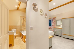 Ein Badezimmer mit Dusche, Toilette und Waschbecken; ein Schlafzimmer mit Bett, Kommode und Fenster; und ein Flur mit einer Tür zum Badezimmer.