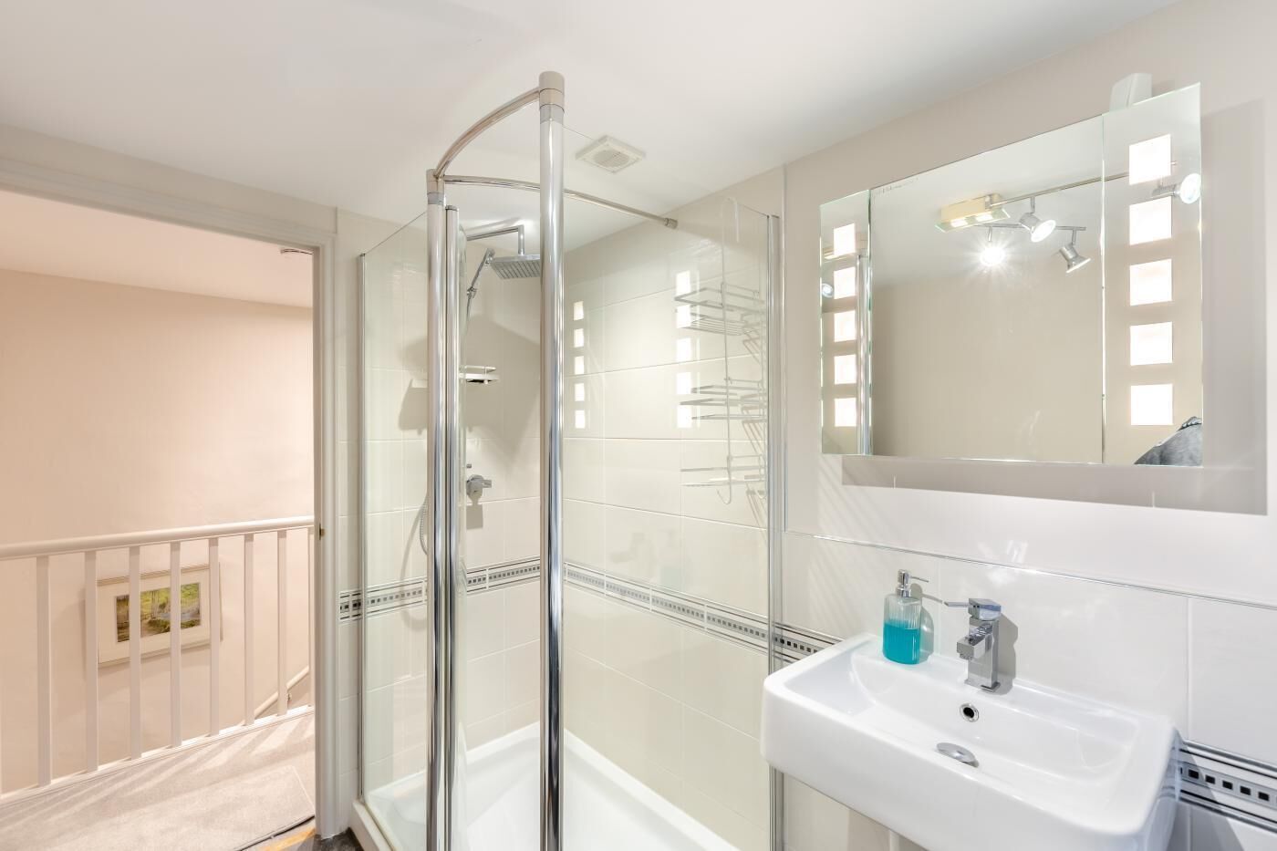 Ein modernes Badezimmer mit Duschkabine aus Glas, einem weißen Waschbecken mit Spiegel und einem Balkon mit Geländer.
