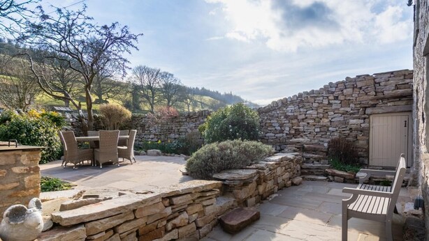 A stone-walled courtyard with outdoor furniture, a stone bench, and a door. - 3 Bed in Gunnerside (oc-t28301) (Satron)