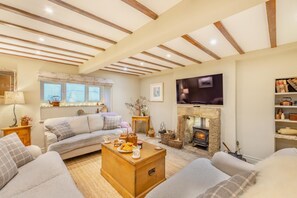 A cozy living room with a sofa, a wooden coffee table, a fireplace, and a television mounted on the wall.