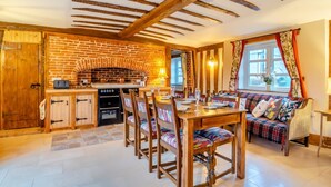A cozy kitchen with a brick wall, wooden beams, and a dining area with a table and chairs. - 3 Bed in Gressenhall (oc-s28418) (Gressenhall)