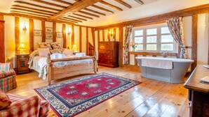 A bedroom with a wooden ceiling, a bed with floral bedding, a red patterned rug, a wooden dresser, and a clawfoot bathtub. - 3 Bed in Gressenhall (oc-s28418) (Gressenhall)