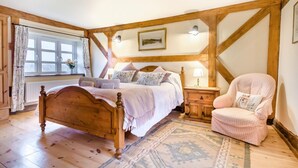 Une chambre confortable avec un lit en bois, une chaise, une table de chevet et une fenêtre avec des rideaux.