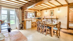 Une cuisine rustique avec des poutres en bois, un coin repas avec des chaises en bois et une vue par la fenêtre.