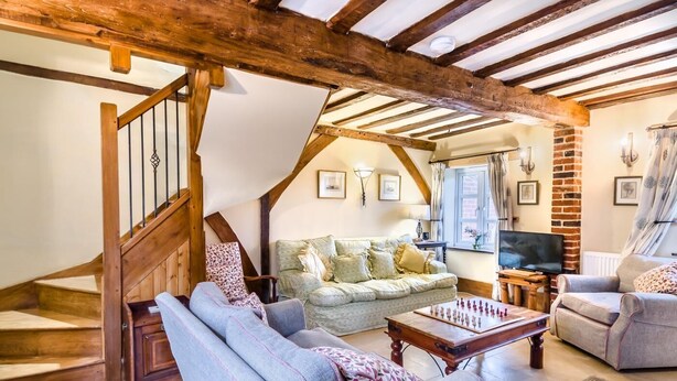 Un salon chaleureux avec un escalier en bois, un confortable ensemble de canapés, un téléviseur et un jeu d’échecs.