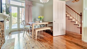A dining area with a wooden table and chairs, a bench, a vase with flowers, and a view through a glass door to the outside. - 3 Bed in Southwold (oc-s28416) (Southwold)