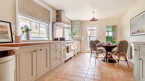 A kitchen with a dining area, featuring light-colored cabinets, a tiled floor, and a window with a view of the outside. - 3 Bed in Southwold (oc-s28416) (Southwold)