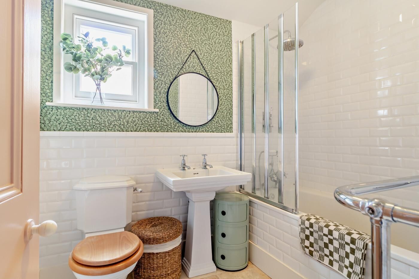 A bathroom with a white toilet, a sink, a mirror, a shower with glass doors, and a window with a plant.