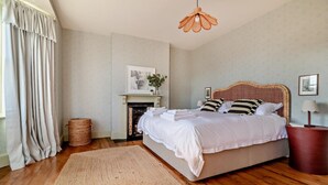 A bedroom with a large bed, a fireplace, a hanging light fixture, and a view of the outdoors. - 3 Bed in Southwold (oc-s28416) (Southwold)