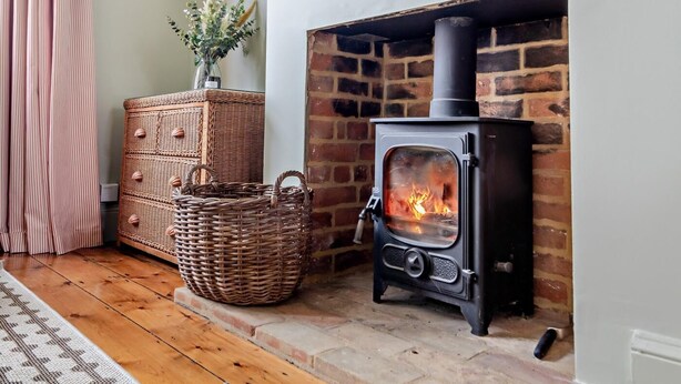 A room with a brick fireplace, a black wood-burning stove, wicker baskets, and a vase with flowers. - 3 Bed in Southwold (oc-s28416) (Southwold)