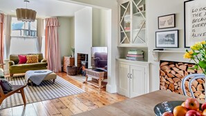 A cozy living room with a fireplace, a sofa, a dining table with fruit, and a bookshelf. - 3 Bed in Southwold (oc-s28416) (Southwold)