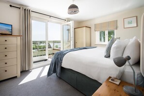 Ein Schlafzimmer mit Bett, Schreibtisch, Lampe, Kommode und Blick ins Freie.