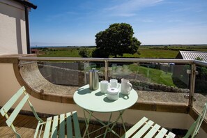 Ein Balkon mit einem für Tee gedeckten Tisch, mit Blick auf eine ländliche Landschaft.