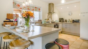Een moderne keuken met een centraal eiland, barkrukken, een roestvrijstalen afzuigkap en een raam met bloemen gordijnen.
