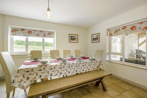 A dining area with a table set for four, a bench, and two windows with floral curtains. - 5 Bed in South Raynham (oc-w28428) (South Raynham)
