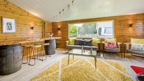 Een gezellig chalet binnen met houten inrichting, een bar met krukken, een bank met kussens en een raam met uitzicht op groen.