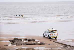 A lifeguard vehicle on a beach with rocks and people in the water. - 4 Bed in Nottage (oc-t28401) (Nottage)