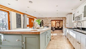 A kitchen with a stone wall, wooden cabinets, and a central island. - 4 Bed in Nottage (oc-t28401) (Nottage)