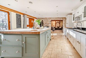 A kitchen with a stone wall, wooden cabinets, and a central island. - 4 Bed in Nottage (oc-t28401) (Nottage)