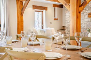 A dining area with a table set for a meal, a sofa in the background, and a stone wall. - 4 Bed in Nottage (oc-t28401) (Nottage)