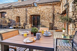 A stone building with a patio area featuring outdoor seating, a table with breakfast items, and potted plants. - 4 Bed in Nottage (oc-t28401) (Nottage)